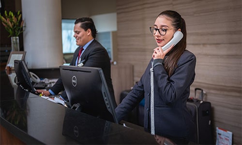 Hotel front desk clerk receptionist on phone by computer